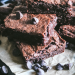 stack of brownies made with fresh milled flour on parchment paper next to chocolate chips.